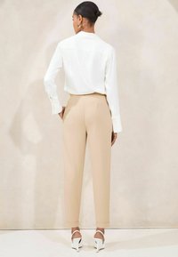 Witte blouse met lange mouwen, gecombineerd met beige taps toelopende broek, met een gladde textuur. Schoeisel bestaat uit witte sandalen met hak en enkelbandjes.