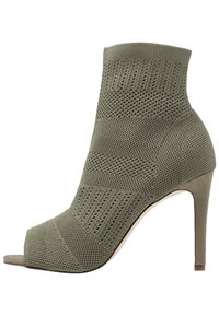 Bottine couleur olive avec orteil ouvert, fabriquée en maille texturée. Présente un talon aiguille élégant et un design à coupe haute côtelée.