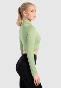 Ribbad, långärmad, kort topp i ljusgrön; har en hög halsringning och en kroppsnära passform. Matchas med svarta högmidjade leggings.