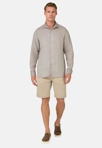 Camicia grigia chiaro con bottoni e maniche lunghe, abbinata a pantaloni corti beige e scarpe slip-on marroni. Outfit casual, che mette in mostra un design confortevole.
