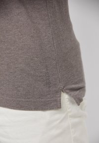 Chemise texturée marron à coupe décontractée, avec une fente latérale et un détail logo subtil à l'ourlet. Associée à un pantalon blanc.