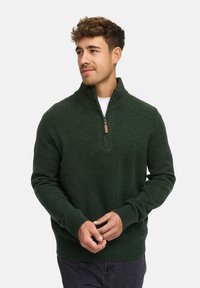 Donkergroen sweatervest met een hoge kraag en halve rits, geribde mouwen en zoom, gemaakt van een gestructureerde brei stof.