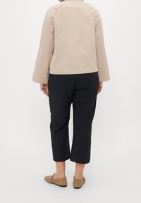 Beige jacka med kort ärm och rak skärning, i kombination med svarta kapade byxor. Platta, ljusbruna skor fulländar outfiten.