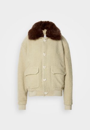 Veste en polaire beige avec un col en fausse fourrure marron, fermeture à boutons à l'avant et deux poches plaquées. Texture douce avec un design décontracté.