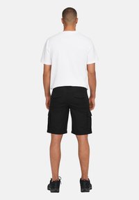 Pantaloni cargo neri con due tasche laterali, tasche posteriori e una maglietta bianca semplice. L'outfit è completato da scarpe sportive nere.