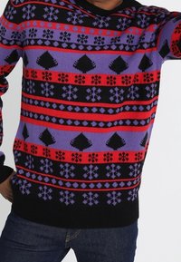 Stickad tröja med svarta, lila, röda och blå ränder med geometriska mönster, inklusive diamanter och snöflingor. Texturerat tyg.