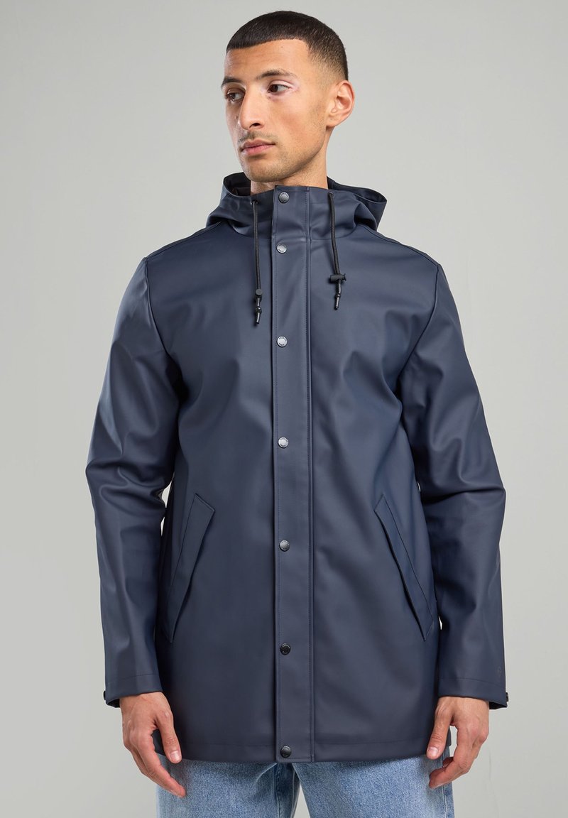 Navy blue waterproof raincoat with a detachable hood, snap closures, adjustable drawstrings, and side pockets. Smooth, durable texture.