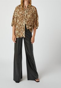 Bluse mit Leopardenmuster und kurzen Ärmeln, locker geschnitten, kombiniert mit schwarzen, weit geschnittenen Hosen aus Kunstleder mit hoher Taille. Schwarze, römische Sandalen.