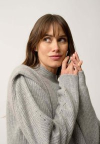 Maglione grigio chiaro a maglia con collo alto e polsini a coste. Caratterizzato da un motivo testurizzato e sottili variazioni di tonalità.