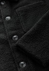 Schwarze Strukturjacke mit Kragen, ausgestattet mit vier runden Kn�öpfen, einer Brusttasche und einem weichen, gewebten Stoff.