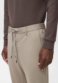 Beige Hose mit elastischem Bund und verstellbarem Kordelzug. Glatte Textur und taillierte Passform; kombiniert mit einem braunen Langarmoberteil.