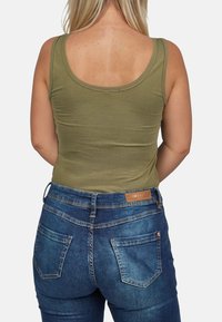 Camiseta de tirantes color verde oliva con escote redondo, combinada con jeans de mezclilla azul que tienen un parche de cuero y dos bolsillos traseros.