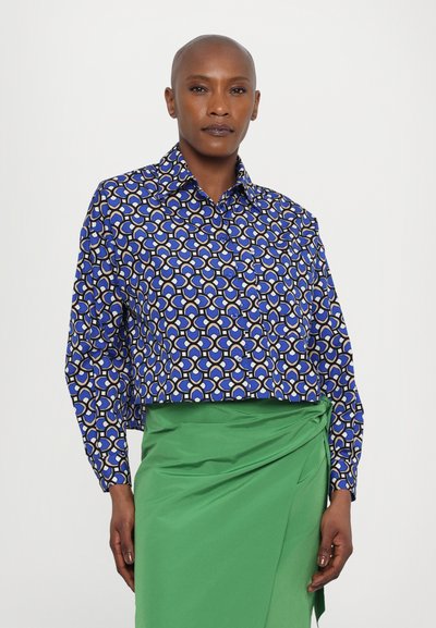 Blue cropped shirt with a geometric pattern in cream and yellow, featuring a pointed collar and button-down front. Paired with a green skirt.