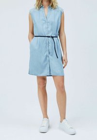 Light blue denim shirt dress with short sleeves, button front, a belted waist, and side pockets. Paired with white sneakers.