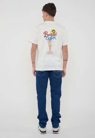 T-shirt bianca in cotone con grafica di un cono gelato e testo "Barrow Cream" in rosso e blu, abbinata a jeans denim blu.