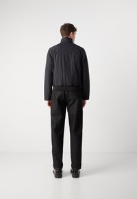 Jachetă puffer neagră cu guler înalt, material texturat, talie elastică și pantaloni gri închis în contrast. Design simplu și modern.