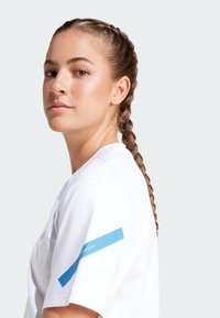 Camiseta deportiva blanca de manga corta, con un acento gráfico azul en el brazo izquierdo y una textura suave similar al algodón.