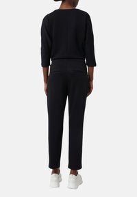 Haut noir à manches trois-quarts et pantalon noir, tous deux en tissu doux, associés à des baskets blanches. Design minimaliste avec des accents subtils.