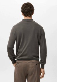 Męski ciemnoszary sweter typu pulower z kołnierzem, długimi rękawami i prążkowanymi mankietami. Gładka faktura; noszony z brązowymi spodniami z tylnymi kieszeniami.