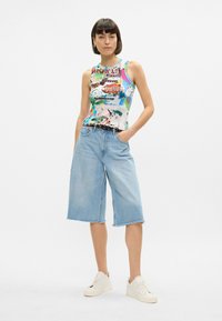 Χρωματιστό αμάνικο μπλουζάκι με γραφικό σχέδιο, συνδυασμένο με ανοιχτό μπλε τζιν culottes. Λευκά αθλητικά παπούτσια ολοκληρώνουν την εμφάνιση.