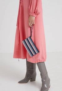 Striped clutch with navy and pink glittery stripes, attached wrist strap. Worn with a long pink dress and gray knee-high boots.