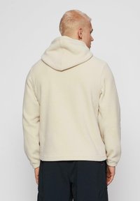 Crème fleece hoodie met een trekkoordkap, een ontspannen pasvorm en lange mouwen, met een gladde textuur en zonder zichtbare patronen of hardware.