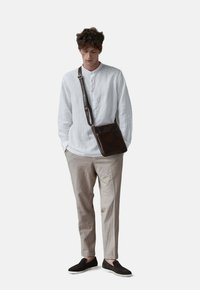 Bílá lněná košile s dlouhým rukávem a henley výstřihem; béžové oblekové kalhoty; tmavě hnědá kožená taška přes rameno; černé slip-on boty.