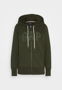 Sudadera con cremallera verde oliva hecha de suave algodón; cuenta con capucha ajustable, bolsillos frontales y la palabra "GAP" en letras de felpa en el pecho.