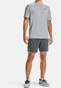 Harmaa kosteutta siirtävä urheilupaita, jossa on hienovarainen kuvio, yhdistettynä tummanharmaisiin shortsseihin, joissa on valkoiset saumat ja Under Armour -logo.