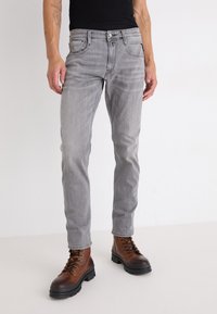 Grå denimjeans med smal passform, som har en klassisk femfickdesign och subtila blekningar, tillsammans med bruna snörstövlar.