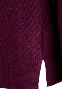 Maglione bordeaux con orlo a coste e motivo testurizzato. Presenta uno spacco laterale per un dettaglio di design aggiuntivo. Realizzato in un materiale morbido e peloso.