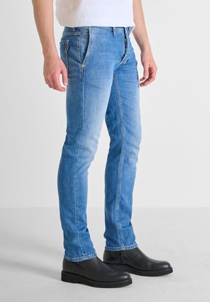 Jeans in denim blu a vestibilità slim con una finitura sbiadita, dotati di tasche frontali, chiusura con bottone e cuciture a contrasto, abbinati a stivali neri.