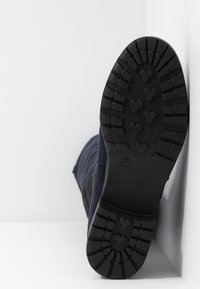 Semelle de botte noire montrant un motif profond de la bande de roulement et la taille 37 sur fond blanc.