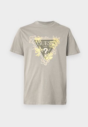 T-shirt in cotone grigio con una grafica triangolare con la scritta "GUESS" e dettagli floreali in giallo. Collo rotondo, maniche corte e vestibilità standard.