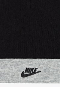 Čierna pletená čiapka s sivým rebrovaným lemom s vyšívaným čiernym logom Nike na prednej strane. Materiál pôsobí mäkko a textúrovaný.