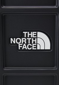 Crna teksturirana površina s istaknutim bijelim logotipom "THE NORTH FACE." Sadrži uzdignutu nijansu oko logotipa za kontrast.
