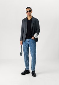 Gray blazer with notched lapels, black t-shirt, blue jeans, and black shoes. Accessories include sunglasses and a gray crossbody bag.