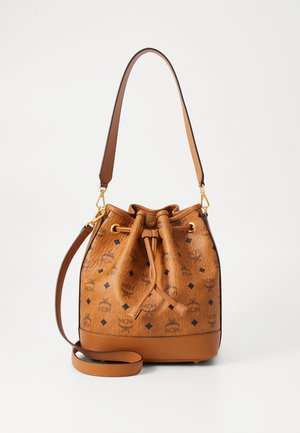 Borsa a secchiello in pelle tan con chiusura a coulisse, accentuata da dettagli in oro e dal motivo del logo MCM in nero. Presenta una tracolla removibile.