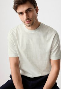 Lys grå tekstureret t-shirt med et diskret stribet mønster, korte ærmer og rund halsudskæring, parret med mørkeblå bukser.