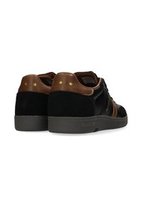 Sneakers in suede e pelle nera con tallone marrone, accenti dorati a forma di stella e suola grigia testurizzata. Presentano un marchio audace sul lato.