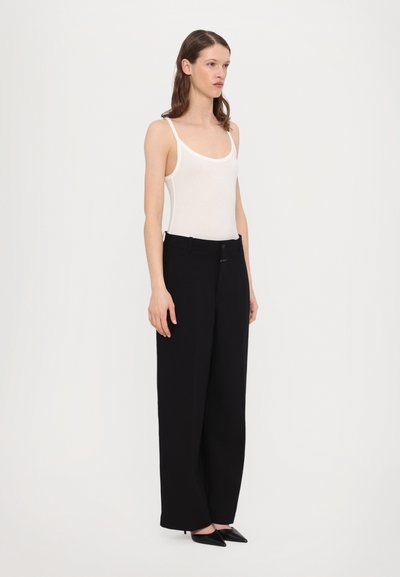 Black wide-leg trousers with a button closure and belt loops, paired with a fitted white tank top. Smooth fabric with minimal texture.