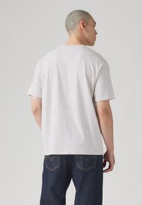 Light gray t-shirt with a textured, speckled pattern, short sleeves, and a crew neck, paired with dark blue denim jeans featuring subtle stitching.