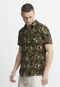 Camisa de manga corta en color verde oliva con un atrevido patrón floral abstracto en blanco y azul marino. Presenta un cuello tipo button-down y un bolsillo frontal.