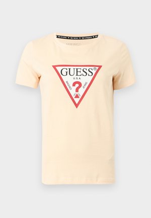 Tricou de bumbac de culoarea piersicii deschise, cu decolteu rotund, mâneci scurte și un logo grafic triunghiular „GUESS” în roșu și negru pe partea din față.