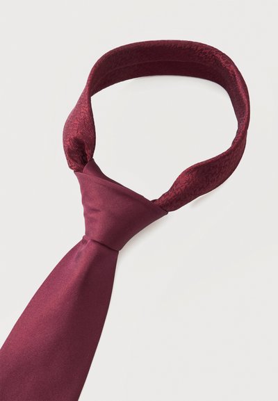 Cravate en satin bordeaux avec un motif texturé tissé sur la bande bouclée et un nœud lisse, soigneusement noué sur fond blanc.
