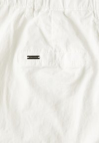 White shorts with a smooth texture, featuring a back pocket and a small metallic logo tag. Simple, clean design without patterns.