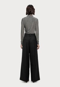 Metallischer Longsleeve in Grau mit figurbetonter Silhouette; hochgeschnittene schwarze weit geschnittene Hose mit Knopfdetails und Gesäßtaschen.