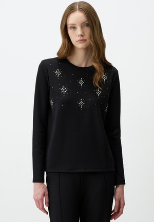 Black long-sleeve top featuring glittering embellishments in a floral pattern. Smooth texture with a classic crew neckline, paired with black trousers.