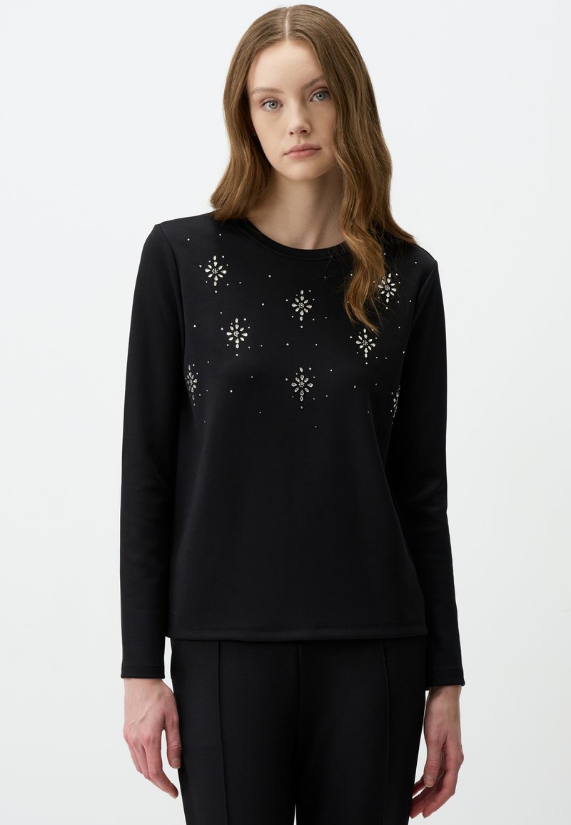 Maglietta nera a maniche lunghe con decorazioni brillanti in un motivo floreale. Tessuto morbido con scollatura classica a girocollo, abbinata a pantaloni neri.