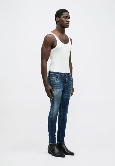 Biela tielko, modré distressed denim džínsy, priliehavého strihu, minimalistický dizajn, skombinované s čiernymi členkovými čižmami. Prítomné sú jednofarebné farby a textúry.